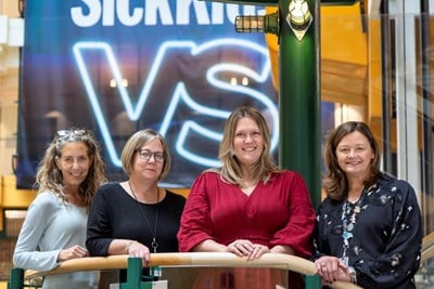 Four advanced practice nurses at SickKids stand together on a staircase landing in front of a blue banner that reads, “SickKids VS”.