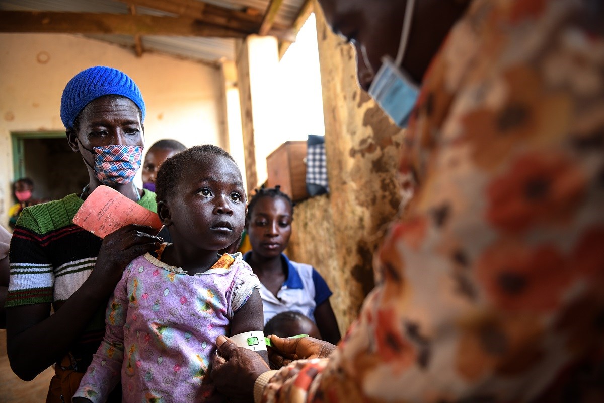 Photo credit: Nutrition International. An HSA is captured measuring MUAC on a girl while her mother looks on at a makeshift clinic in Kapise Village, Mwanza, southern Malawi.