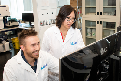 Two people in white lab coats looking at a computer.