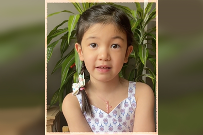 Child sits in front of a plant. The backdrop is repeated and blurred on the sides.