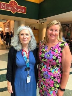 Kristina, wearing a pink dress, stands next to Dr. Diane Herbert, who wears a blue dress. The photo is taken at Main Street at SickKids.