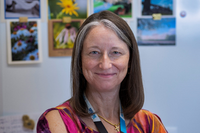 Clinical Nurse Specialist Lee-Anne Pires smiles in front of a light blue background with images of flowers and skylines.