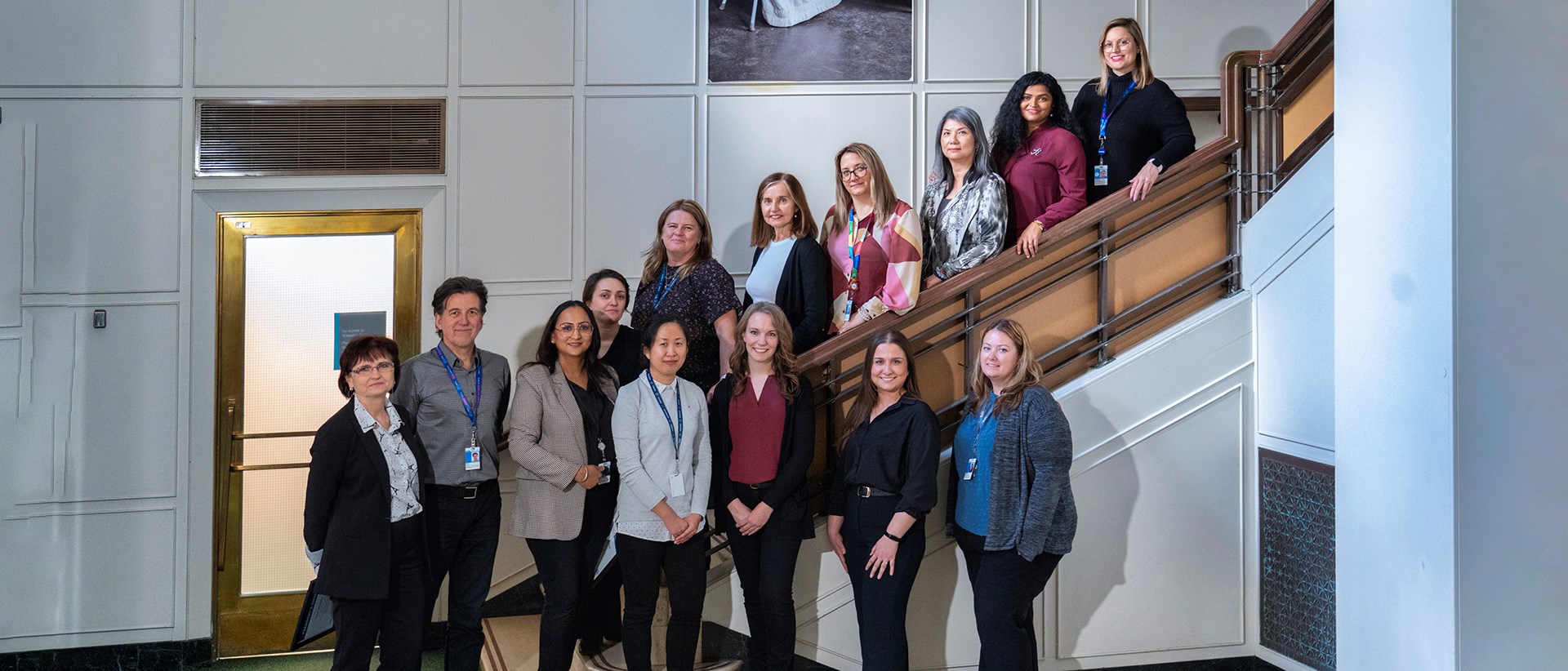 A group of 14 individuals standing together for a photo. Some are standing the steps of a staircase.
