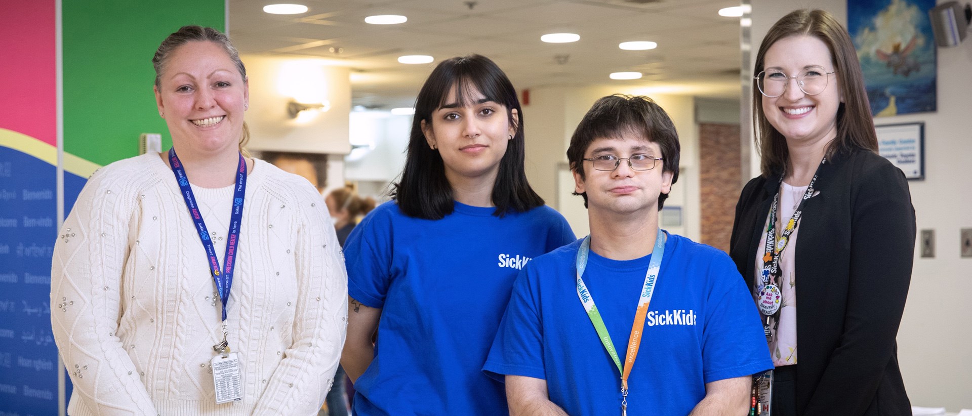 Four people standing together for a photo. Two individuals are wearing blue SickKids t-shirts.