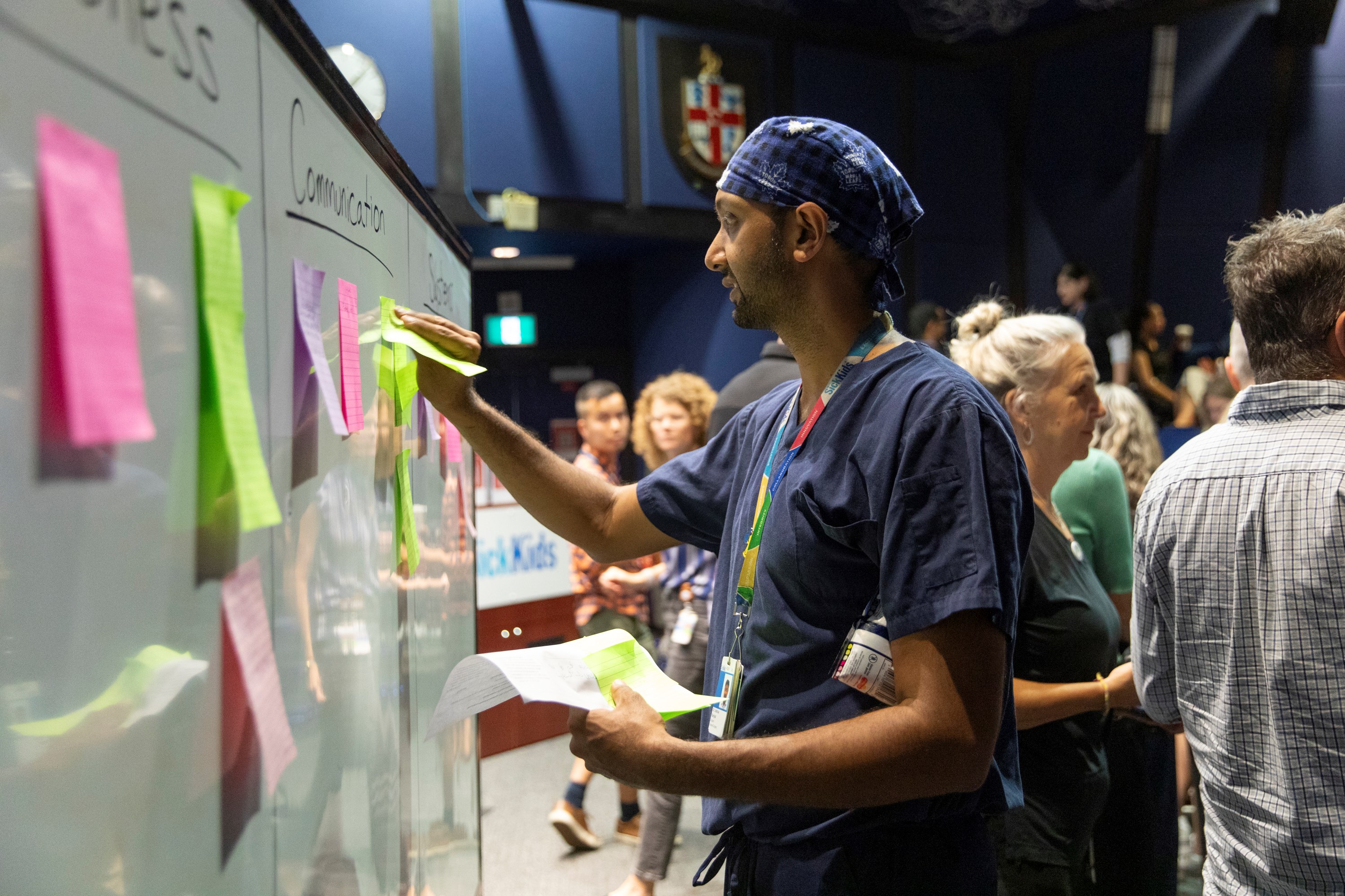 Dr. Joshua Ramjist reviews notes made by staff regarding areas for discussion during the Code Orange simulation debrief session in front of a white board full of sticky notes.
