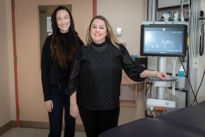 Lauren Lauren Erdman and Mandy Rickard stand next to an ultrasound machine in the Urology Clinic at SickKids.