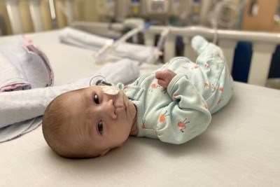 A baby lying on bed. There is hospital equipment in the background.