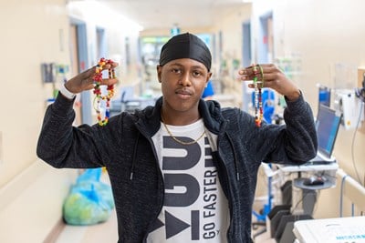 A young man standing in a hospital hallway holding colourful Bravery Beads in his hands.