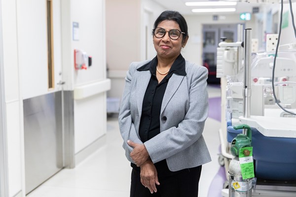 Dr. Savithiri Ratnapalan, wearing a black collared shirt and grey blazer, stands in a hallway in the emergency department.