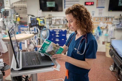 Dr. Deborah Schonfeld rests The Hospital for Sick Children Handbook of Paediatrics against a laptop on a stand in a trauma room in the emergency department.
