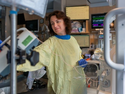 Yevel, a nurse, checks a monitor in a NICU room while dressed in a personal protective gown.