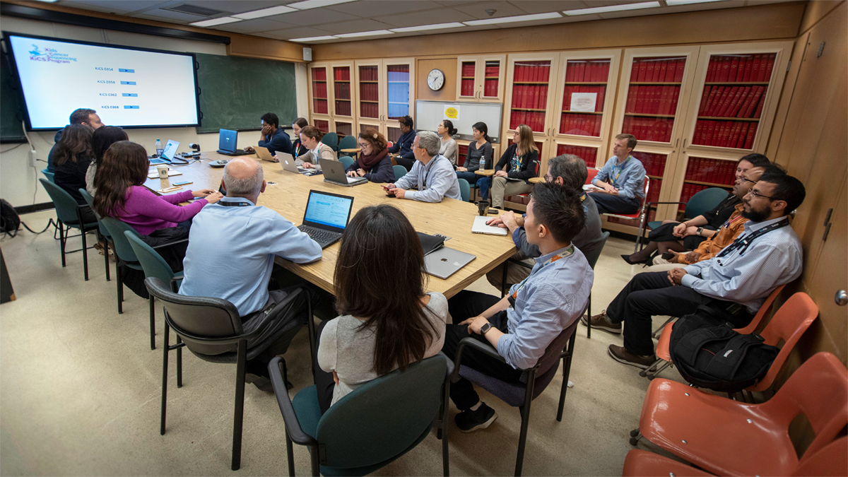 Members of a Molecular Tumour Board meeting seated in a conference room review a care on a screen