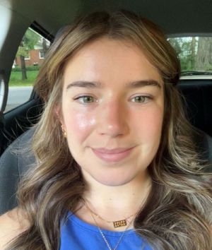 Caelan Ferguson is shown from the shoulders up in the passenger seat of a vehicle wearing a blue top and smiling. 