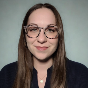 Francesca Salvador is depicted in a headshot from the shoulders up in front of a gray background. She is wearing a black shirt and glasses.