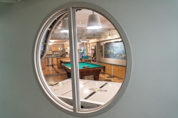 A circular window shows an air hockey table and pool table in Marnie's Lounge. 