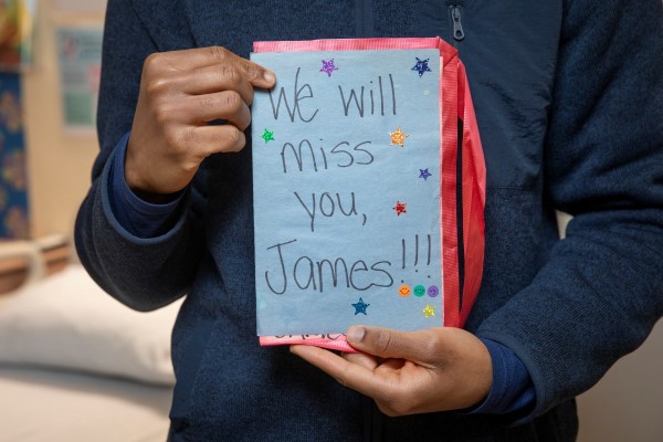 James holds a blue handmade card that reads " We will miss you James."