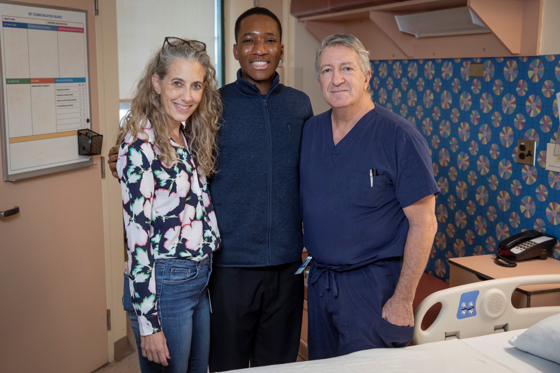 James stands between Charis and Joel in a room on unit 8C.
