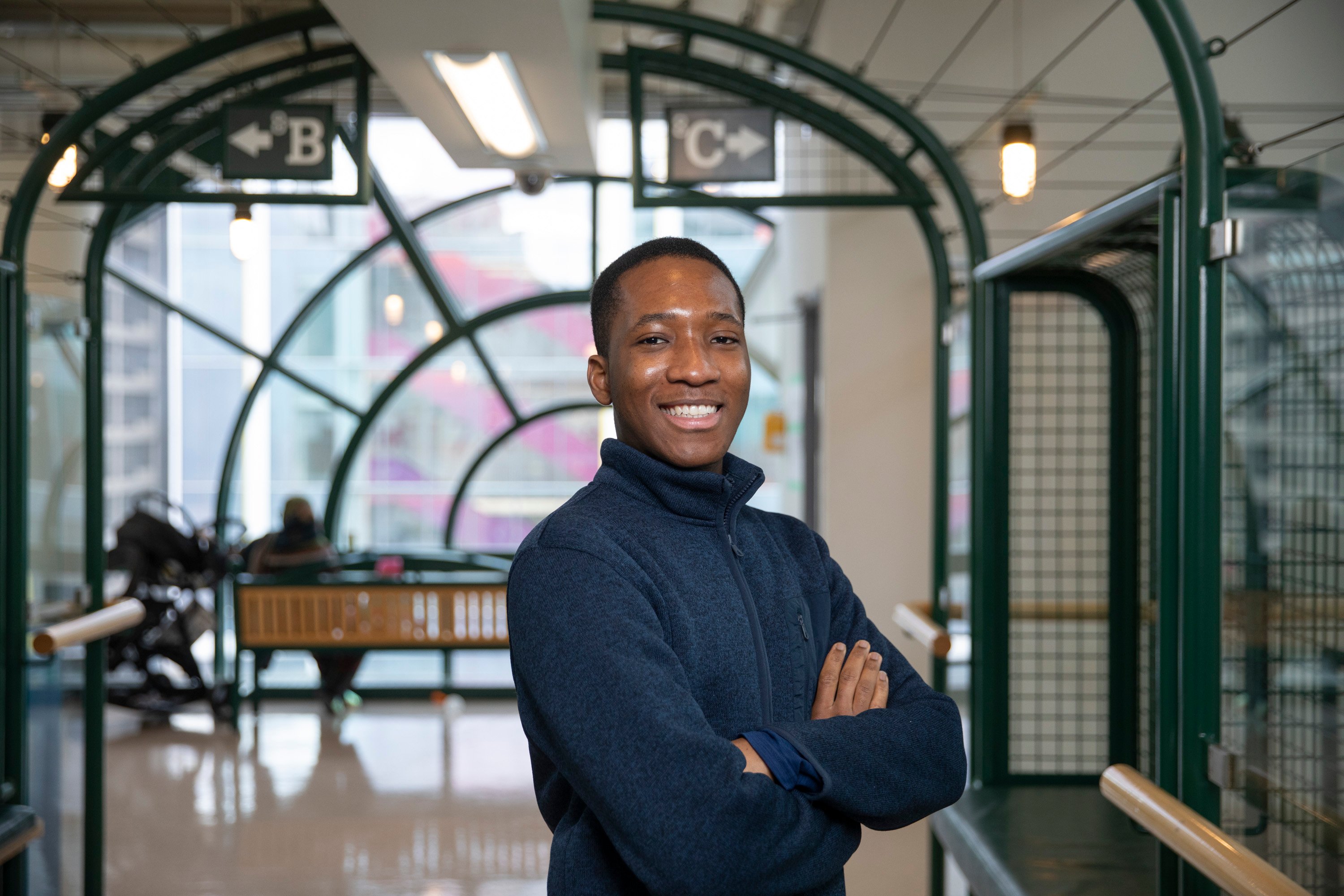 James, wearing a navy blue sweater, stands in the hallway with signs for units 8B and 8C behind him.