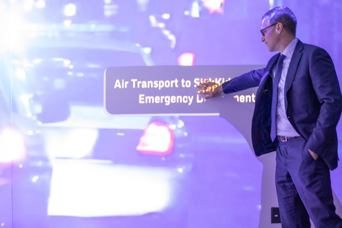 A person gestures toward a large immersive display showing an emergency air transport scenario at SickKids