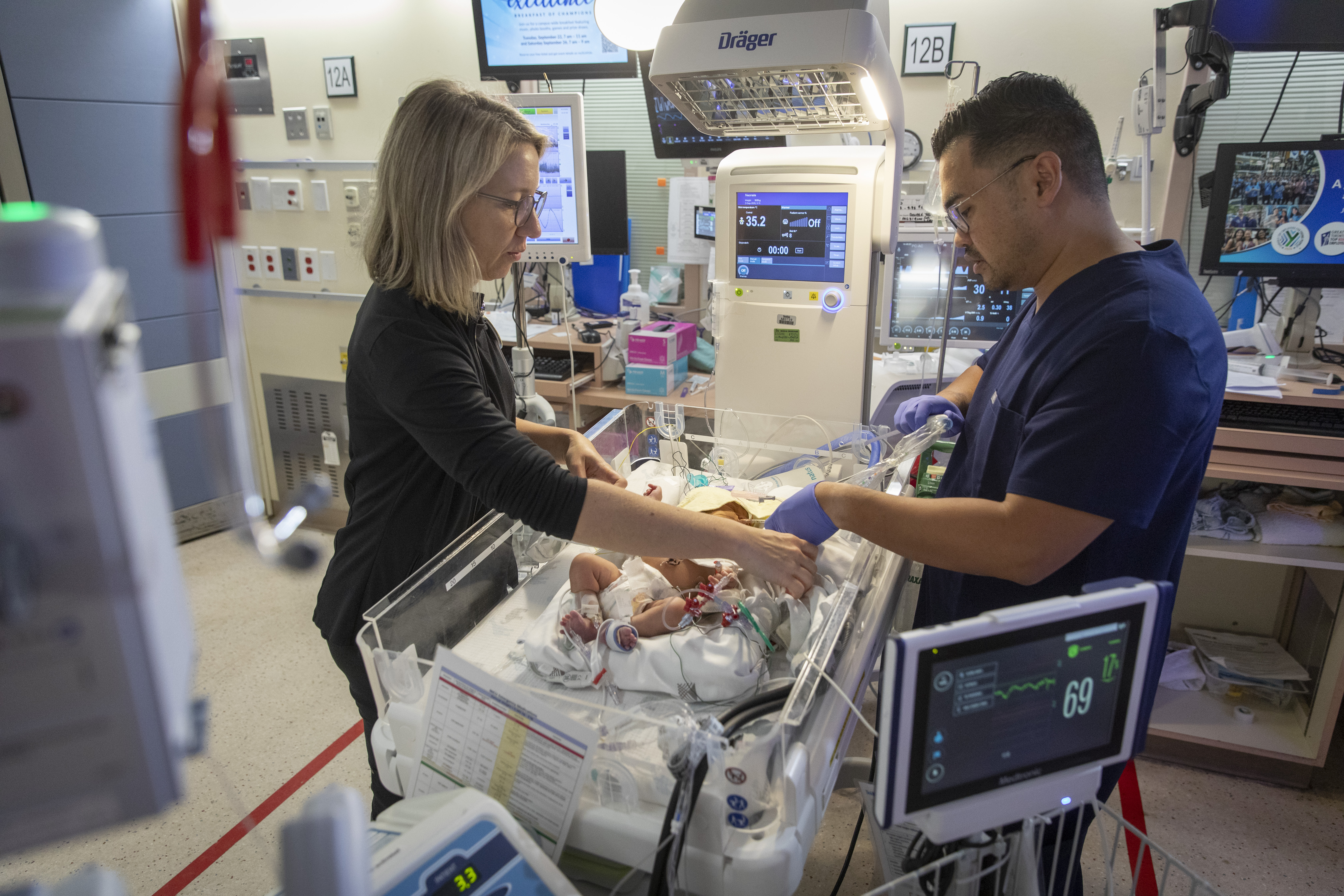 Two nurses look over a NICU crib and care for a patient.