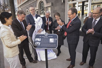 A group of adults stand around a historical plaque clapping and smiling
