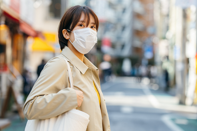 Person wearing a mask and holding a tote bag while walking on the street.