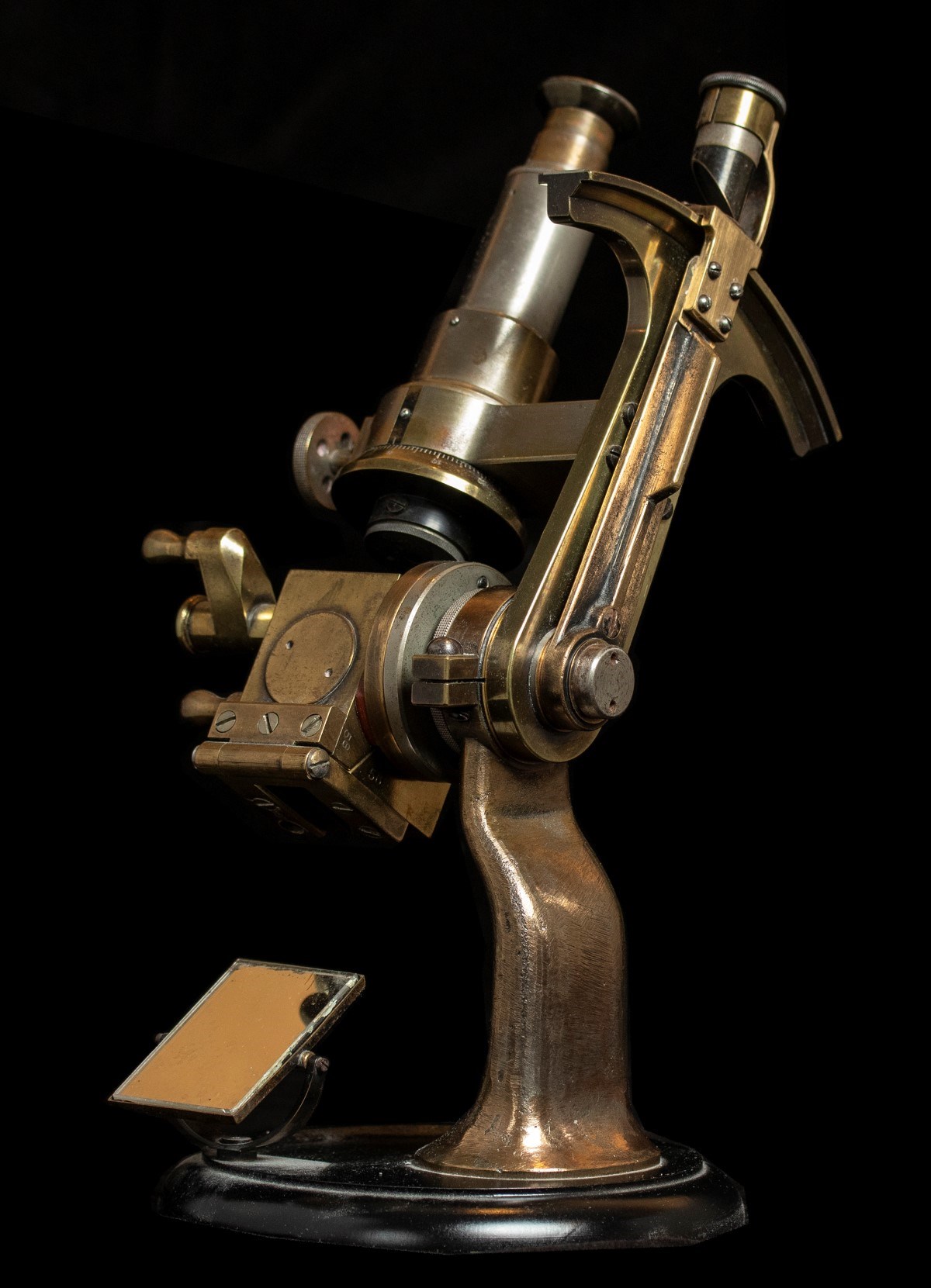 Three-quarter view of an Abbe refractometer made of a worn brass-like metal. The instrument resembles a microscope with an eyepiece at the top and a slanted platform at the bottom to place the sample.