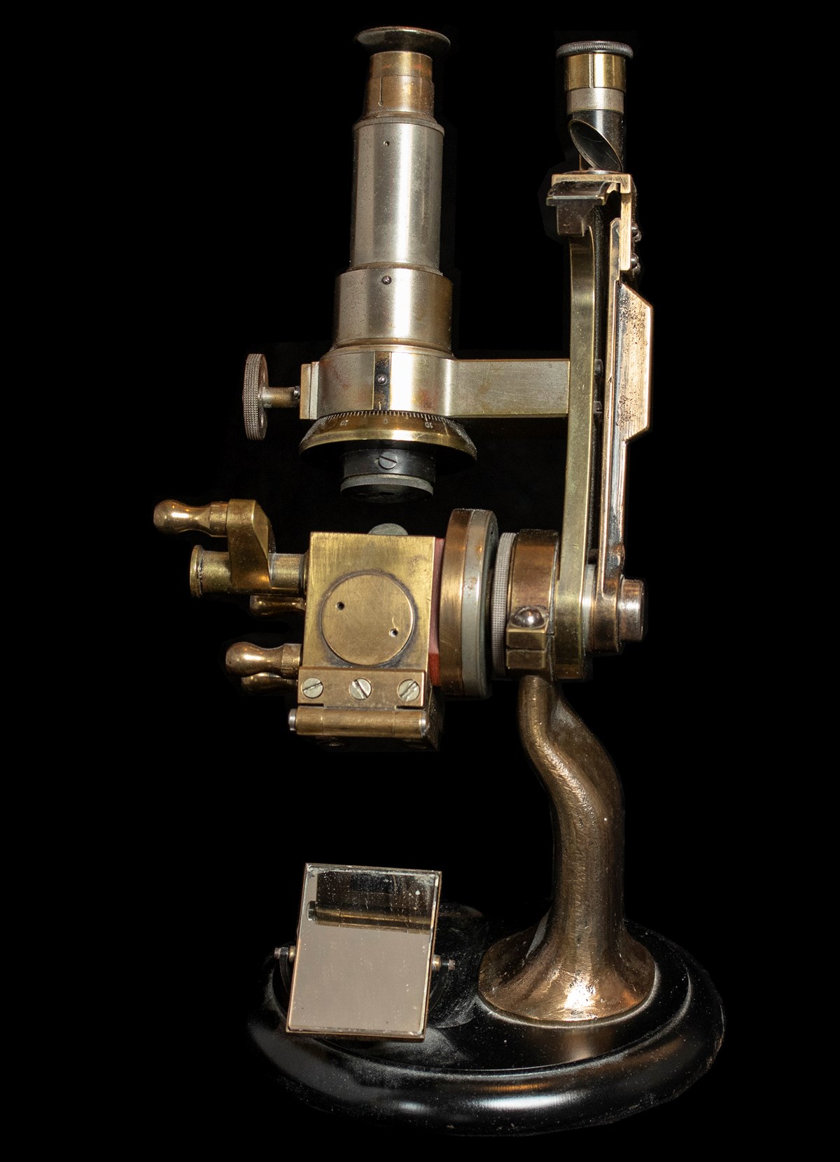 Front view of an Abbe refractometer made of a worn brass-like metal. The instrument resembles a microscope with an eyepiece at the top and a slanted platform at the bottom to place the sample.