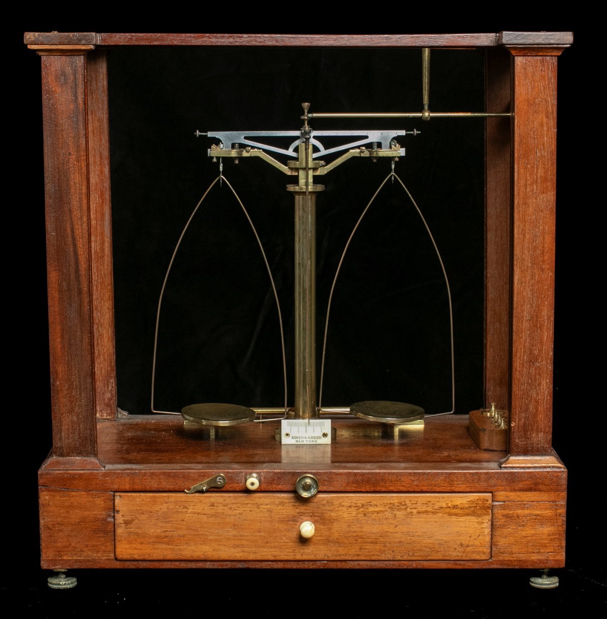 An apothecary scale consisting of two brass metal balances. The scale is inside an antique wooden display case.