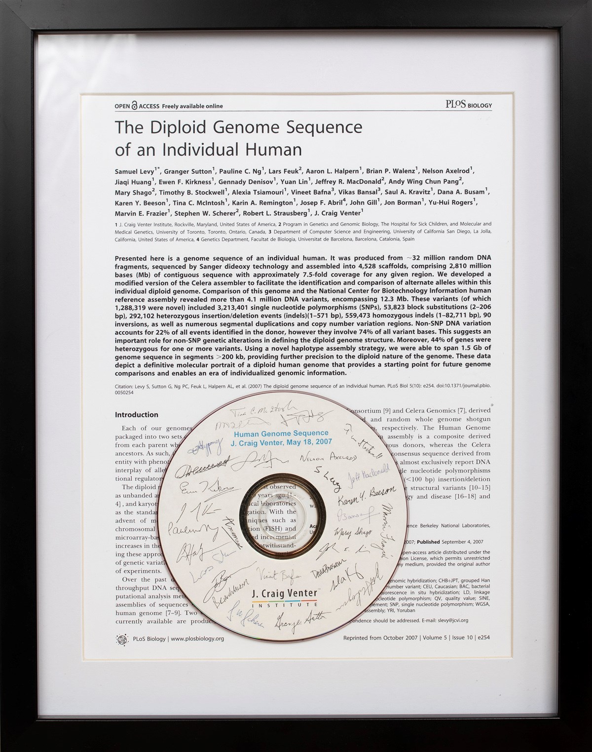 A framed copy of the first page of the publication "The Diploid Genome Sequence of an Individual Human". Inside the frame, there is also a CD that reads "Human Genome Sequence, J. Craig Venter, May 18, 2007". The CD is signed by many individuals.