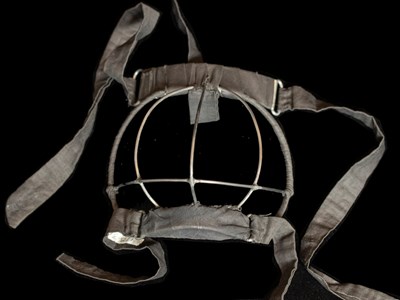 A mask made of cloth straps to secure around a child's head and a metal wire piece that goes over the bottom half of the child's face that prevents them from eating lead paint.