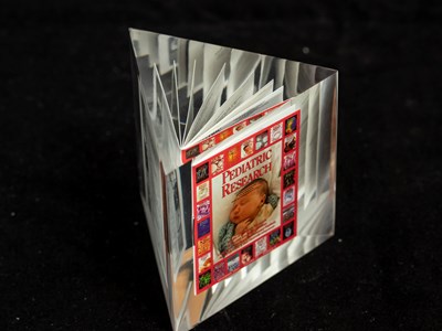 A copy of the 'Pediatric Research' journal encased in a glass prism. The cover of the journal features a sleeping infant.